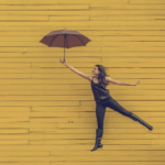 Woman with umbrella floats on yellow board wall